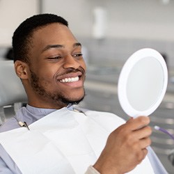Man smiling at reflection in handheld mirror