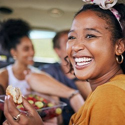 Woman smiling while eating meal with friends in car
