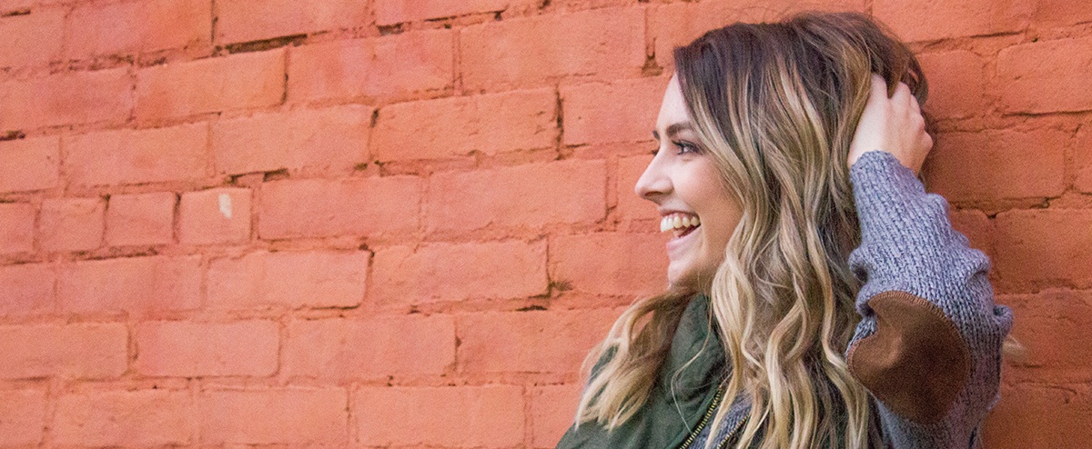 Woman with beautiful smile standing against brick wall