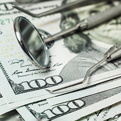 Dental tools laying on a pile of hundred-dollar bills