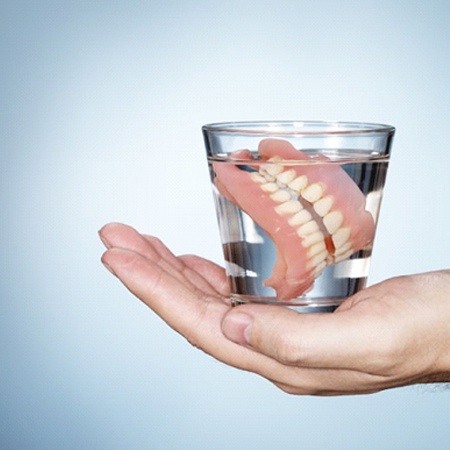 hand holding dentures in glass of water