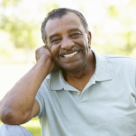 Man with mustache smiling while sitting outside
