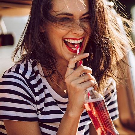 Laughing woman drinking from a glass soda bottle