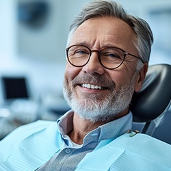 older man smiling with dental apron on in the dentist’s chair