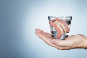 hand holding glass of water with dentures soaking in it