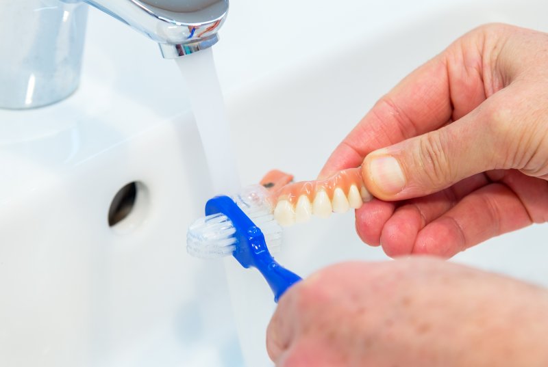 Person caring for dentures using a denture brush