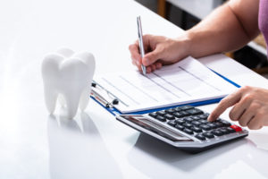 White Tooth on Desk In Front Of Man Using Calculator